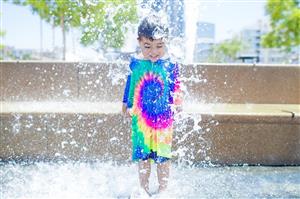 Smiling Boy Playing With A Water Sprinkler